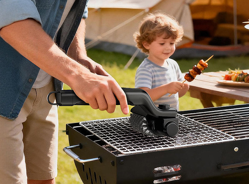 Hand using a black electric grill brush to clean a BBQ grill